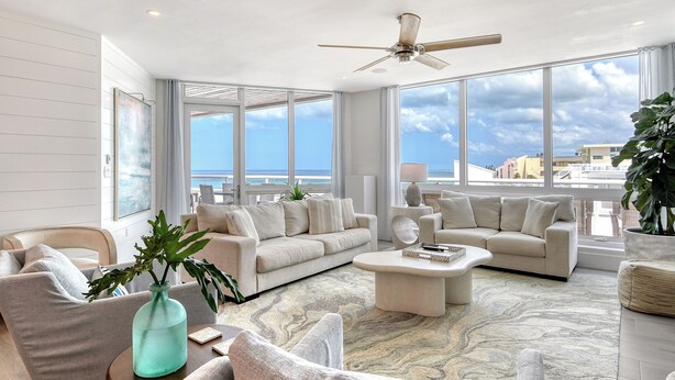 Tilava olohuone, jossa on suuri ikkuna, josta avautuu näkymä merelle ja kaupunkimaisemaan.