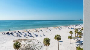 Ein Strand mit weißem Sand, blauen Sonnenschirmen und Palmen.