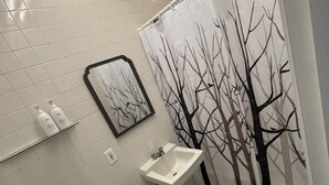 A bathroom with a toilet, sink, and shower curtain with a tree design. There is a framed picture on the wall and a rug with text on the floor.