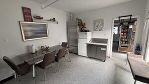 A compact kitchen with a dining area, a refrigerator, a microwave, and a vending machine.