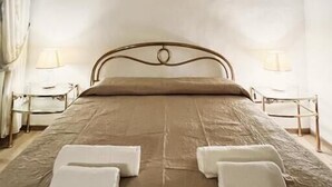 Un dormitorio con cama, dos mesitas de noche, una lámpara de noche, un cuadro en la pared y una ventana con cortinas.