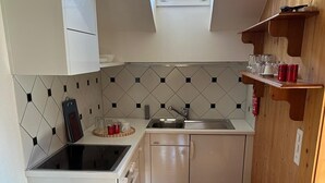 Uma cozinha compacta com claraboia, uma pia e uma prateleira de madeira com copos e enlatados.