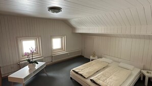 Quarto com cama grande, mesa de cabeceira, radiador e janela com cortinas.