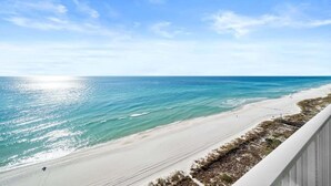 Blick auf einen Strand vom Balkon aus, mit blauem Himmel und ruhiger See.