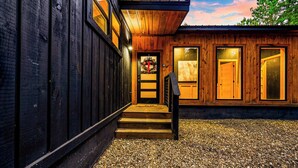 A wooden building with a gravel driveway and a wooden staircase leading to a door with a glass panel. - Swim & Recharge | Heated Pool Spa | Pool Table (Broken Bow)