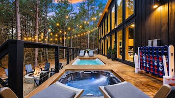Ein moderner Außenbereich mit Whirlpool, Liegestühlen, Pool und Lichterketten.