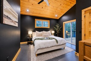 A bedroom with a large bed, two bedside lamps, a window, and a view of the outdoors.