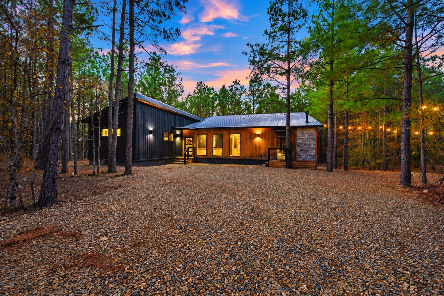 A cabin with a gravel driveway, surrounded by trees, and a stone wall.