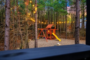 A playground with a slide and swings, surrounded by trees and string lights. - Swim & Recharge | Heated Pool Spa | Pool Table (Broken Bow)