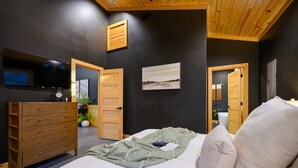 A bedroom with a bed, wooden dresser, a television, and a painting on the wall. - Swim & Recharge | Heated Pool Spa | Pool Table (Broken Bow)