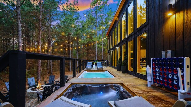 A modern outdoor spa area with a hot tub, lounge chairs, and a pool, surrounded by trees and string lights. - Swim & Recharge | Heated Pool Spa | Pool Table (Broken Bow)