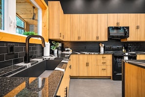 A modern kitchen with wooden cabinets, a black countertop, and a microwave. - Swim & Recharge | Heated Pool Spa | Pool Table (Broken Bow)
