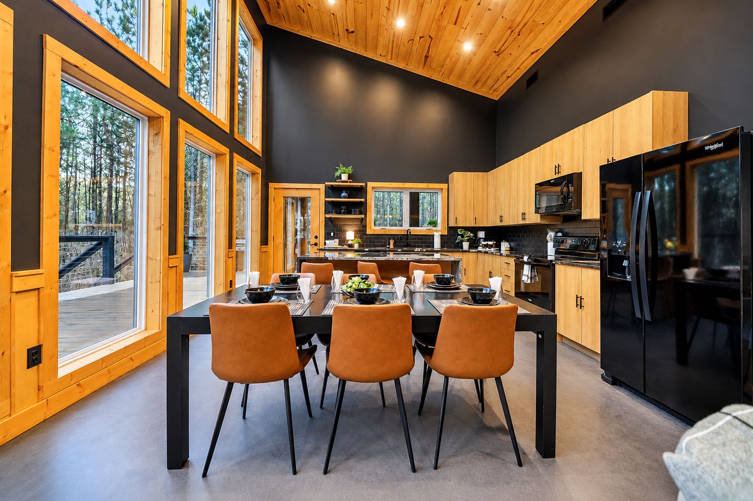 A modern kitchen with a dining area, large windows, and a view of the outdoors.