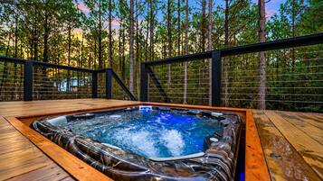 Ein Whirlpool auf einer Holzterrasse, umgeben von einem Metallgeländer, mit einem Wald im Hintergrund.