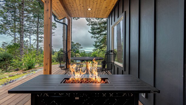 Une table avec foyer intégré, des chaises, une vue sur l’océan et une terrasse en bois.