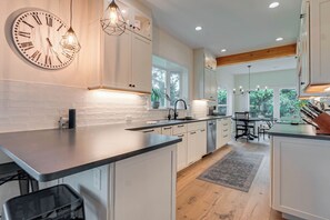 A modern kitchen with a large wall clock, pendant lighting, and a view of the outdoors.