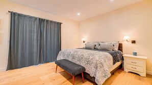 Une chambre à coucher avec un lit, des tables de chevet, un banc et un rideau.