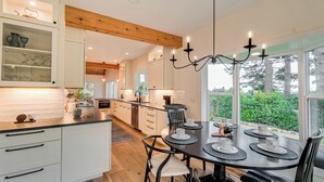 Une cuisine moderne avec des armoires blanches, un plafond en bois et un coin repas comprenant une table ronde et des chaises.