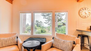 Une pièce chaleureuse avec deux fauteuils, une petite table et une grande fenêtre donnant sur un jardin et des arbres.