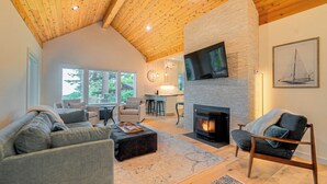 Un vaste espace de vie agrémenté d’une cheminée en pierre, de sièges confortables et de grandes fenêtres offrant une vue sur l’extérieur.
