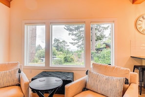 A room with three large windows, a round table, and two armchairs.
