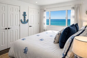 A bedroom with a bed, a view of the ocean, white doors, and a nautical-themed wall decoration.