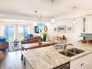 A modern kitchen with a marble countertop, a sink, and a dining area with a table and chairs.