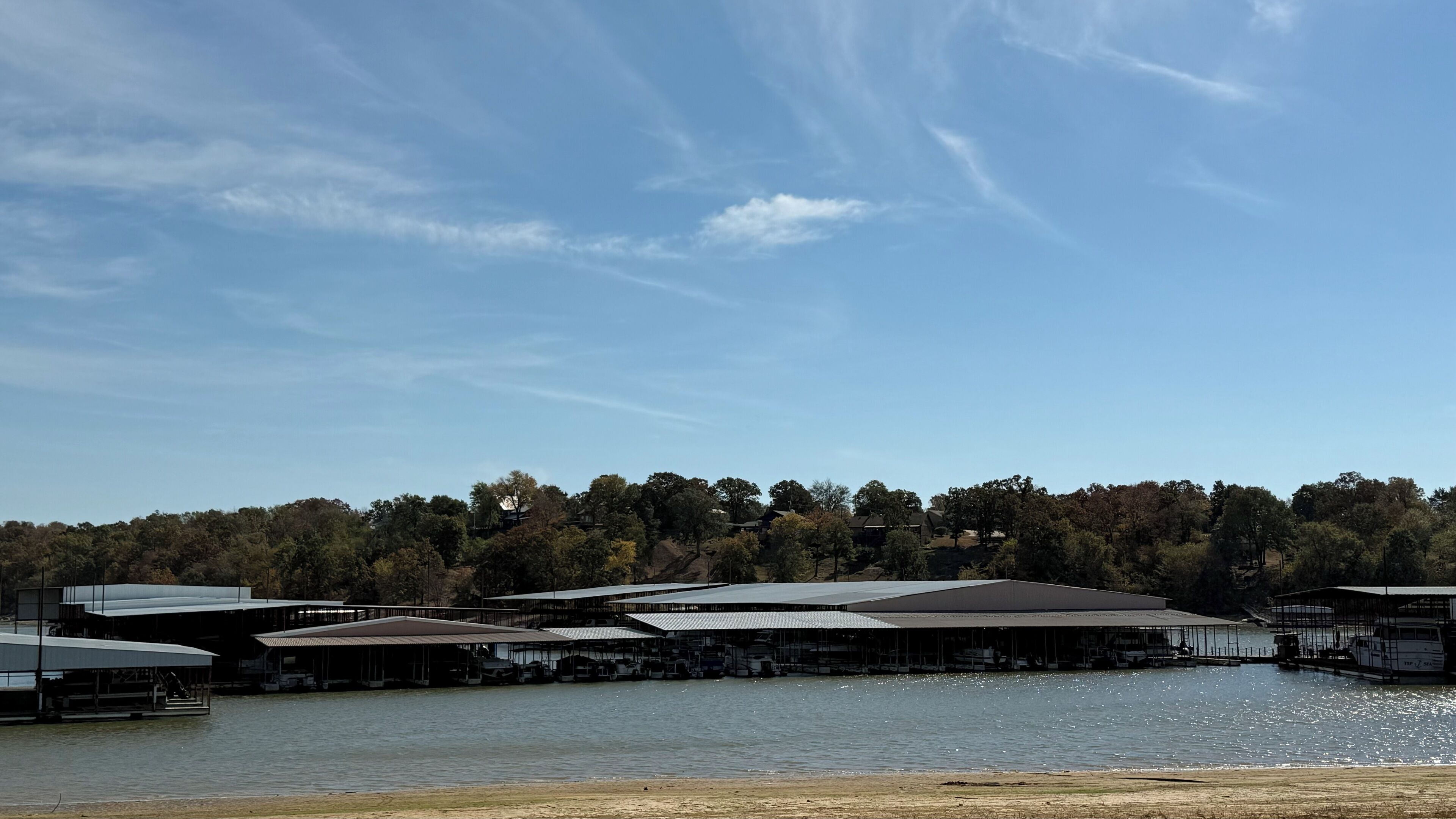 A waterfront property with multiple covered structures, a dock with boats, and a forested hill in the background.
