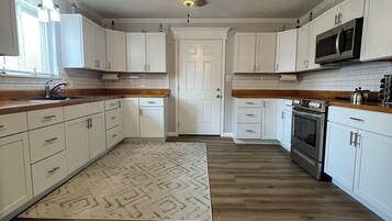 A kitchen with white cabinets, a wooden countertop, a ceiling fan, and a microwave.
