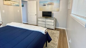 A bedroom with a bed, a ceiling fan, a TV on a dresser, and artwork on the walls.
