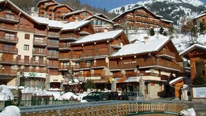 Een skigebied met houten gebouwen, balkons en een besneeuwde berg op de achtergrond.