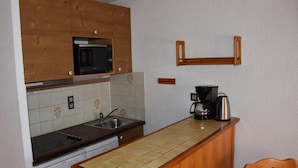 Een kleine keuken met houten kastjes, een magnetron, een koffiezetapparaat en een spoelbak.