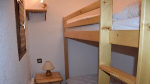 Een slaapkamer met een stapelbed, een houten nachtkastje en een lamp.