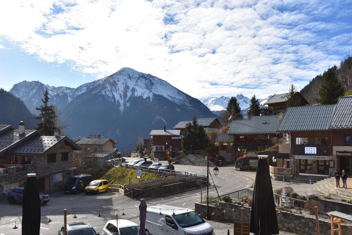A mountain town with traditional buildings, a parking area, and a view of snow-capped mountains.