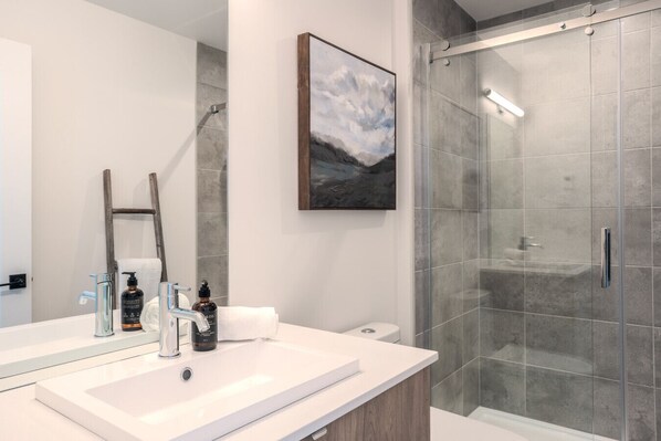 Un baño moderno con un espejo grande, cabina de ducha y una escalera de madera apoyada en la pared.