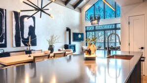 A spacious kitchen with a large island, modern pendant lighting, and large windows offering views of the outdoors. - Tremblant Prestige - Verbier 4-202 (Mont-Tremblant)