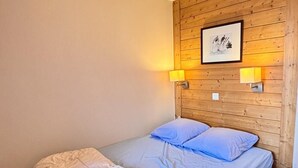 Una cama individual con cabecera de madera, dos lámparas de noche y un cuadro enmarcado en la pared.