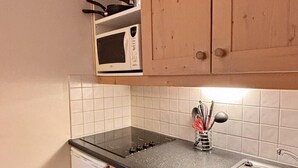 Cocina compacta con gabinetes de madera, microondas, lavamanos y lavavajillas.