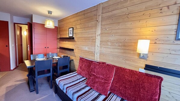 A cozy room with a wooden wall, a bed with striped bedding, a red throw, a dining table with chairs, and a small shelf with a picture. - 10m from ski slopes, 2nd floor, view resort, balcony, tv, ski locker, 24m², Avoriaz (Avoriaz)