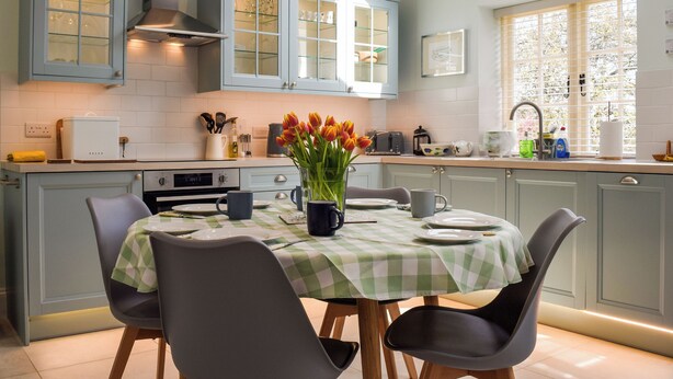 A modern kitchen with light blue cabinets, a dining table with a green and white checkered tablecloth, and a vase of tulips.