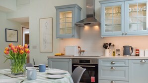 A modern kitchen with light blue cabinets, a stainless steel range hood, and a dining area with a checkered tablecloth.
