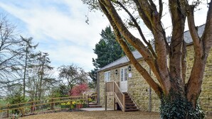 A stone building with a wooden staircase leading to a door, surrounded by gravel and trees.