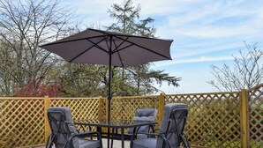 An outdoor patio with a round table and four chairs, a large umbrella, and a wooden lattice fence.