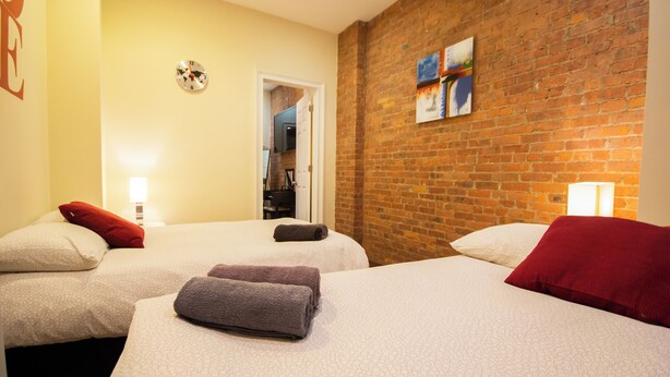Habitación de hotel con dos camas, una pared de ladrillo y una puerta que da al baño.