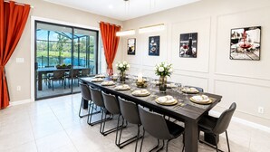 Un espace repas avec une longue table dressée pour six personnes, des chaises et une vue sur l’extérieur grâce à des portes vitrées.