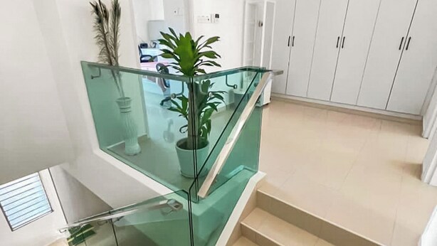 A modern staircase with glass railings and beige steps, leading to a room with white walls and cabinets. - 4 Bedroom Landed House (Batu Pahat)