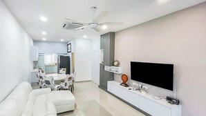 A modern living room with a white sofa set, a coffee table, a flat-screen TV mounted on a white console, and a ceiling fan. - 4 Bedroom Landed House (Batu Pahat)