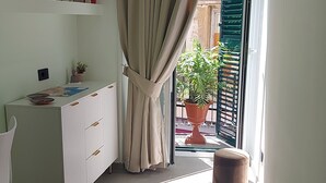 A room with a desk, a chair, a potted plant, and a sliding glass door leading to an outdoor area with a balcony. - PIGNASECCA DOMUS (Naples)