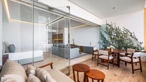 Un espacio moderno con separador de vidrio, un sofá, zona de comedor con sillas y cocina.
