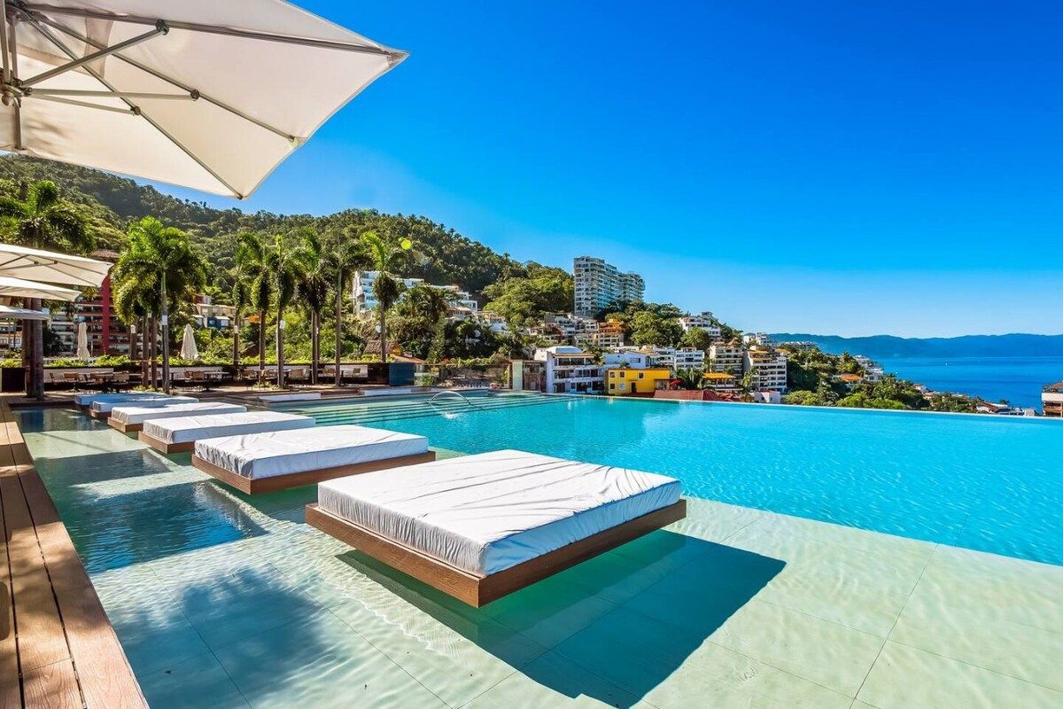 A poolside area with sunbeds and umbrellas, overlooking a coastal cityscape.